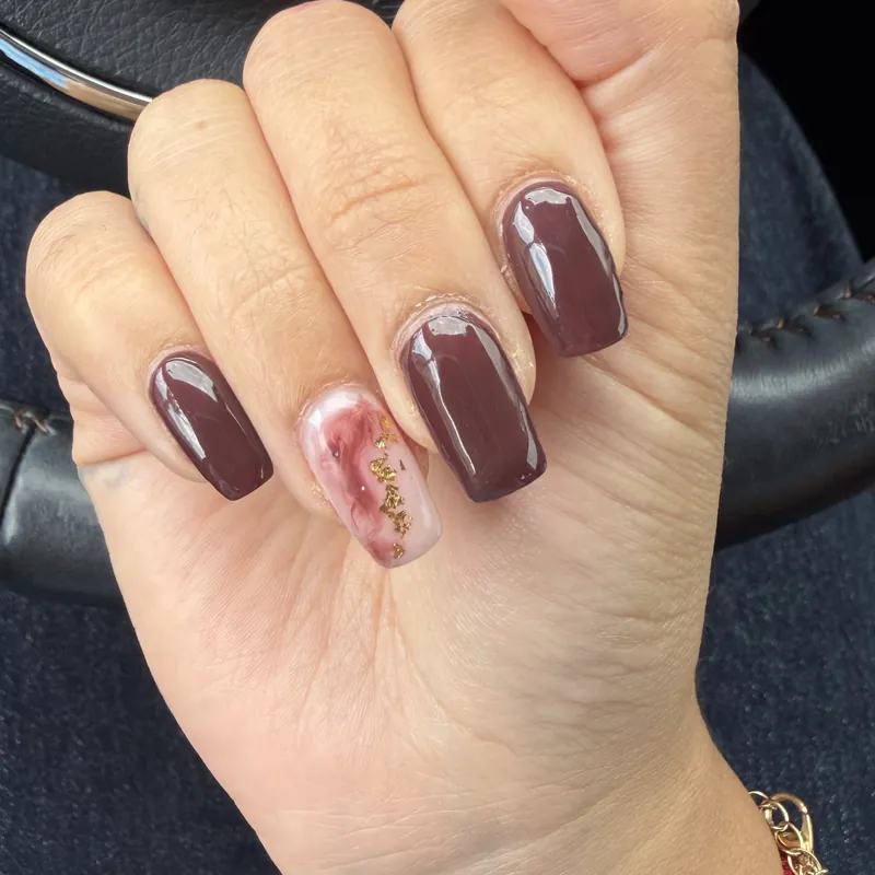 Uñas cuadradas color chocolate con una uña marmolada y pan de oro